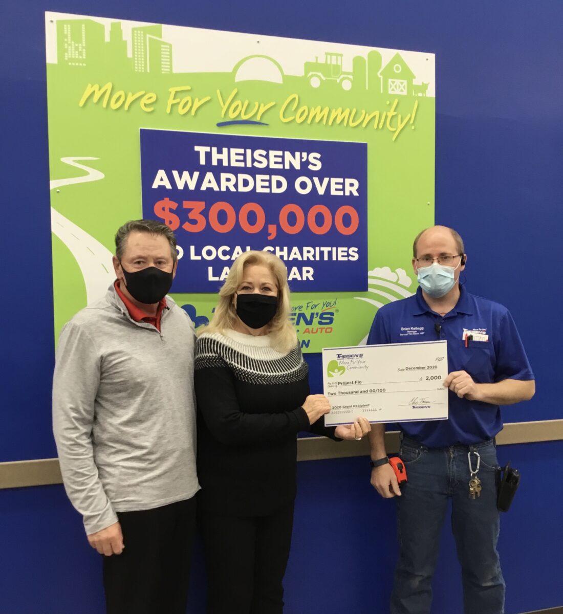 Three people wearing masks stand in front of a sign, holding a large check for $2,000. The check is addressed to The Salvation Army.